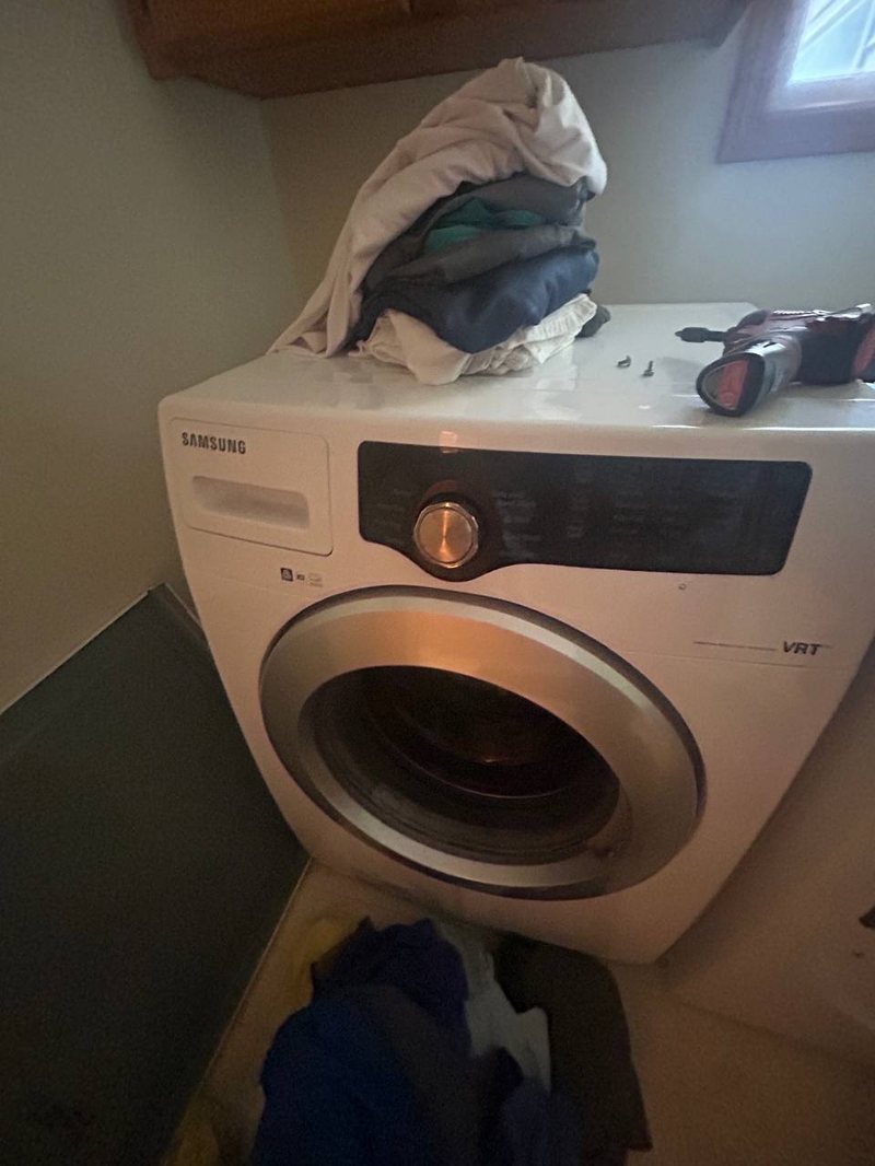 Samsung VRT front-load washer with laundry and a drill on top during a drain pump job